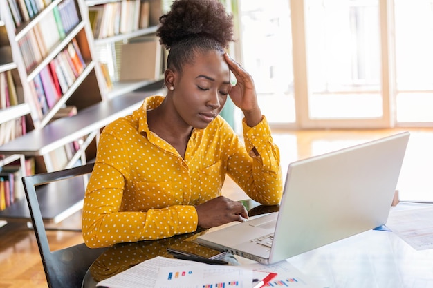 Young frustrated woman working at office desk in front of laptop suffering from chronic daily headaches treatment online appointing to a medical consultation electromagnetic radiation sick pay