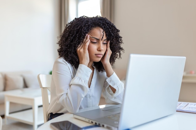 Young frustrated woman working at office desk in front of\
laptop suffering from chronic daily headaches treatment online\
appointing to a medical consultation electromagnetic radiation sick\
pay