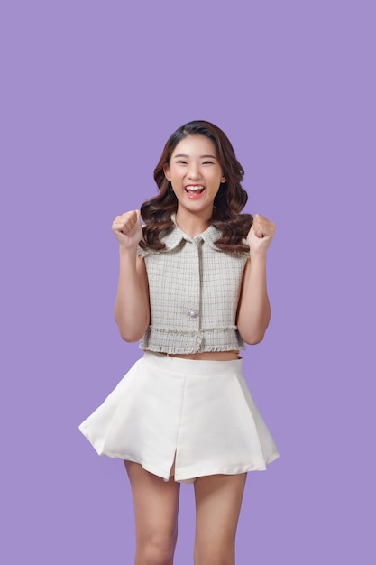 Young fun asian woman doing winner gesture celebrate clenching fists say yes isolated on purple color background