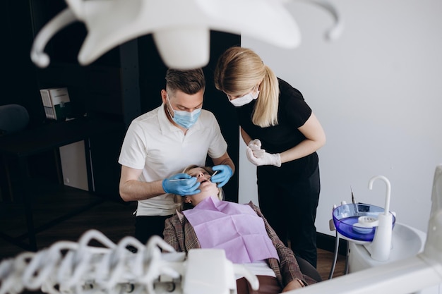 Young fun orthodontist dentist caucasian man wear gown showing jaw bite teeth xray for patient woman sitting at dentist office chair indoor cabinet near stomatologist Healthcare enamel treatment