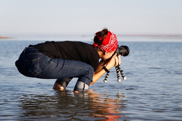 Young fun woman photographer with professional camera in the sea