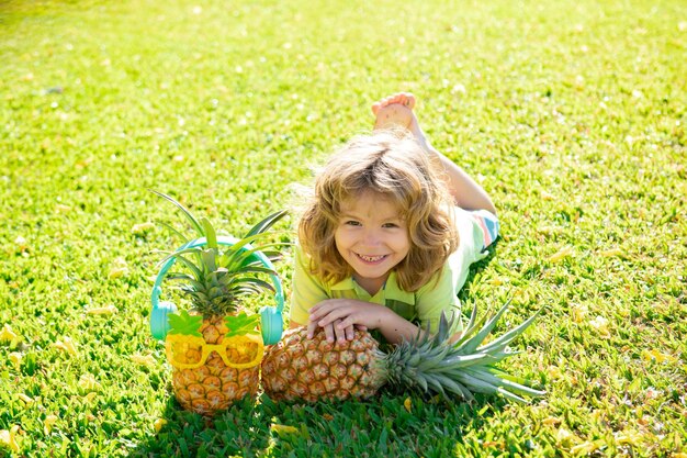 パイナップルを保持し、パイナップルの子供たちの夏の果物と裏庭の子供で笑っている若い面白い男の子