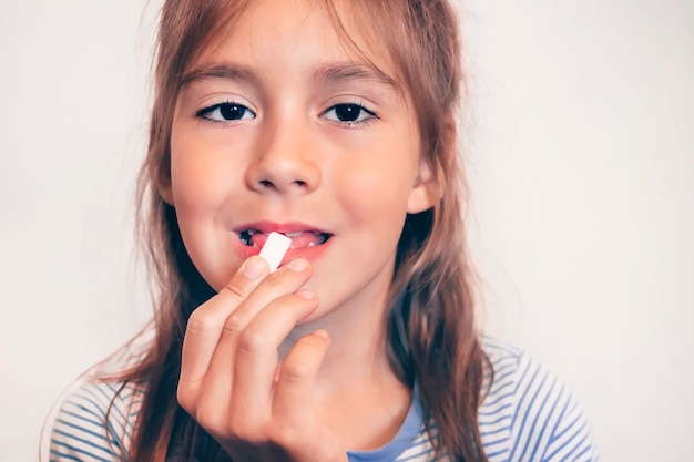 Giovane ragazza divertente con gomma da masticare. alito fresco. alito cattivo. lavarsi i denti dopo i pasti con le gomme. bambino mette la bocca aperta in primo piano gomma cuscino bianco. spazzolare.