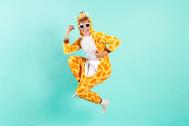 Young funny guy winner in orange giraffe pajamas jumps at the party in sunglasses on blue background