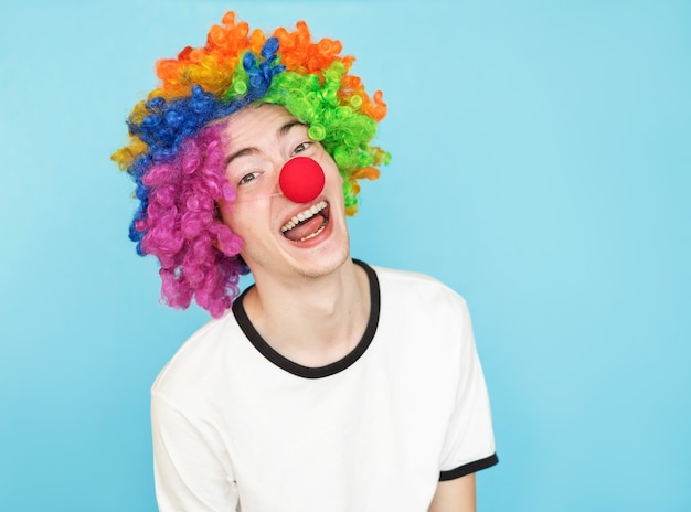 Молодой смешной мужчина-подросток в белой футболке на синем фоне в парике клоуна
