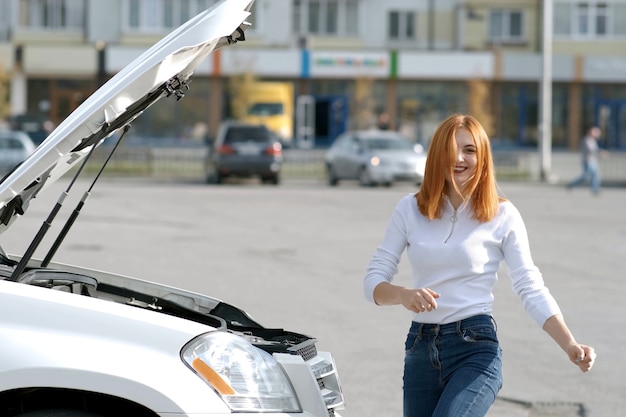 Young funny smiling woman driver near broken car with popped hood