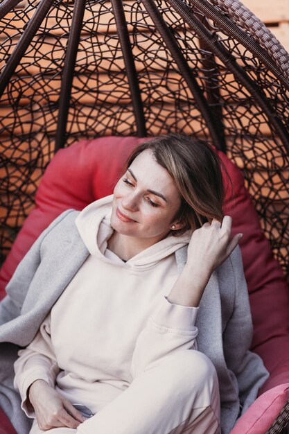 Young funny woman spends time outdoors in a woven chair