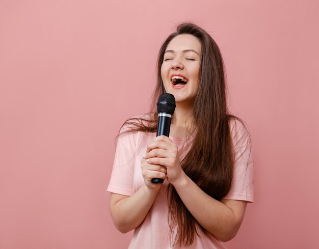 Young funny woman with microphone in hand on pink background