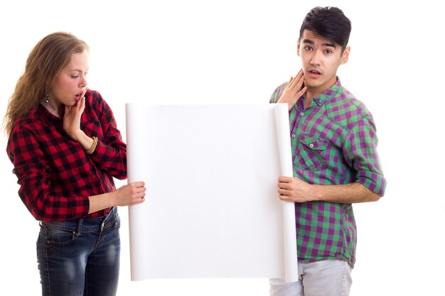 Young funny woman with young handsome man with dark hair in plaid shirts holding white placard