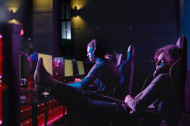 Young gamer relaxing on his chair in front of computer after computer game in dark room of computer club