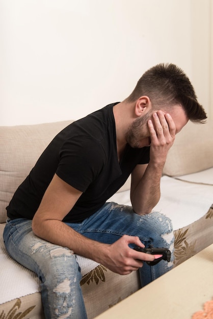 Young Gamer Sitting On Sofa And Playing Video Games At Home