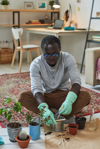 部屋の床に座っている間彼の植物を気遣う若い庭師