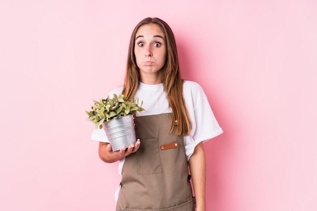 La giovane donna caucasica del giardiniere ha isolato le spalle di scrollate di spalle e gli occhi aperti confusi.