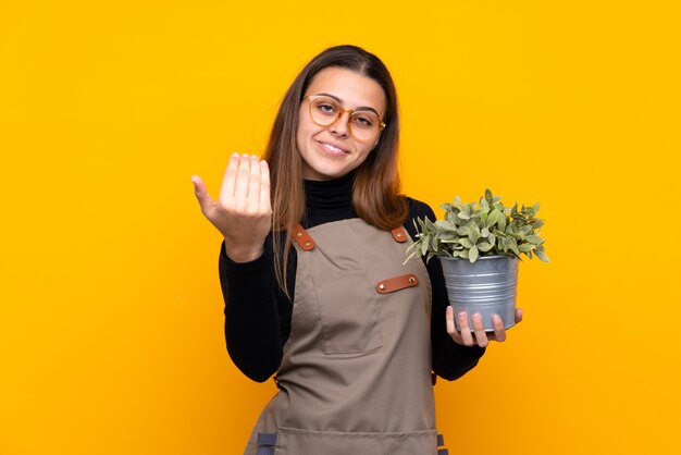 Young gardener girl holding a plant inviting to come