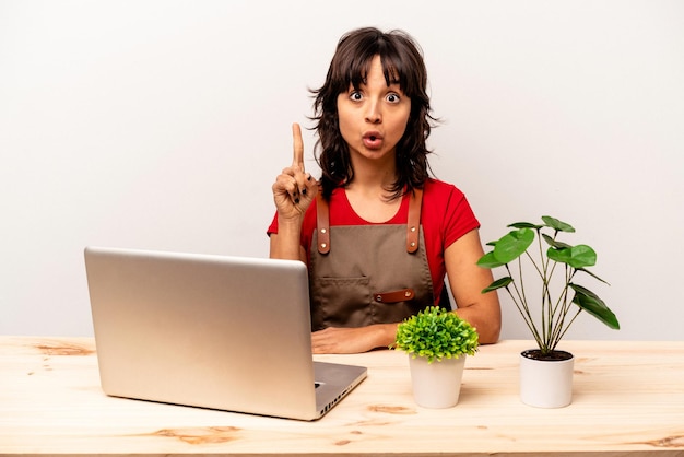 Young gardener hispanic woman sitting on a table isolated on white background having some great idea concept of creativity