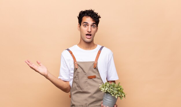 Young gardener man feeling happy, excited, surprised or shocked, smiling and astonished at something unbelievable