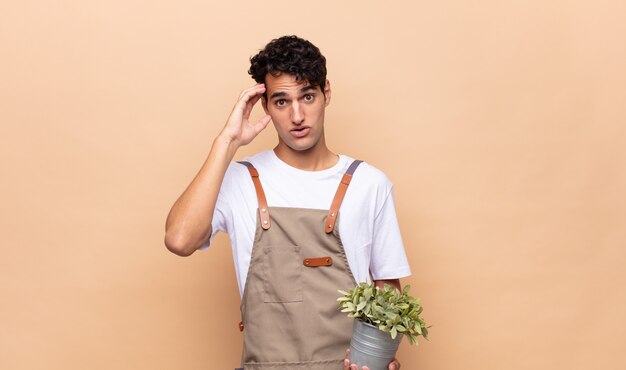 Young gardener man looking happy, astonished and surprised, smiling and realizing amazing and incredible good news