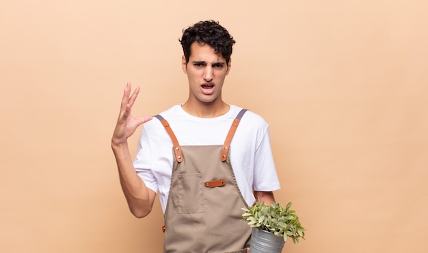 Foto giovane giardiniere che grida con le mani in aria, sentendosi furioso, frustrato, stressato e sconvolto