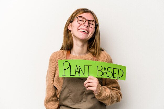 Young gardener woman holding a plan based placard isolated on white background laughing and having fun.