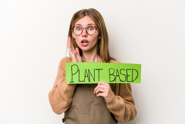 Young gardener woman holding a plan based placard isolated on white background surprised and shocked.