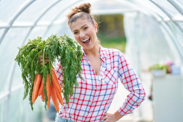 Young gardener woman with carrots in greenhouse