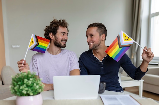 LGBTQ 깃발을 들고 화상 통화로 친구들과 인사하면서 유쾌하게 웃고 있는 젊은 게이 커플