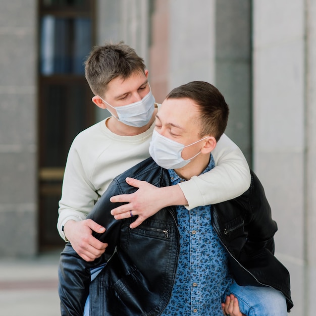 Young gay couple wearing medical mask hugging at city