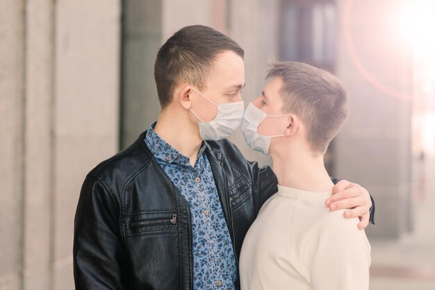 Young gay couple wearing medical mask hugging at the city