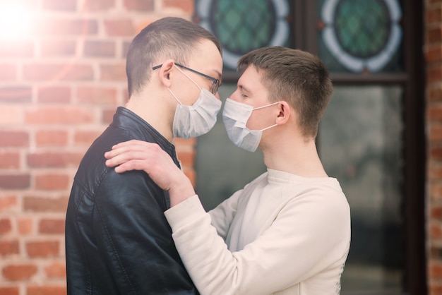 Young gay couple wearing medical mask, hugging and kissing at the city.