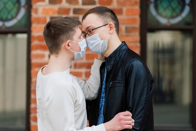 Young gay couple wearing medical mask, hugging and kissing at the city.