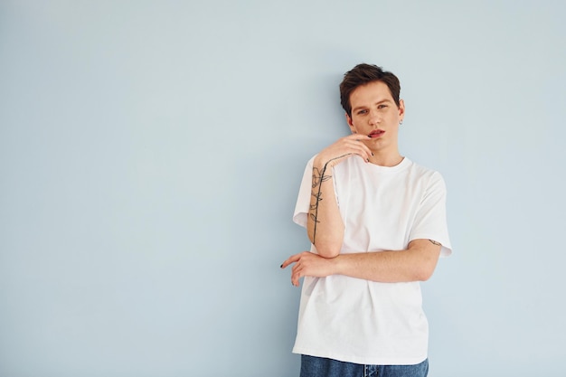 Young gay man is standing in the studio and posing for a camera In casual white shirt