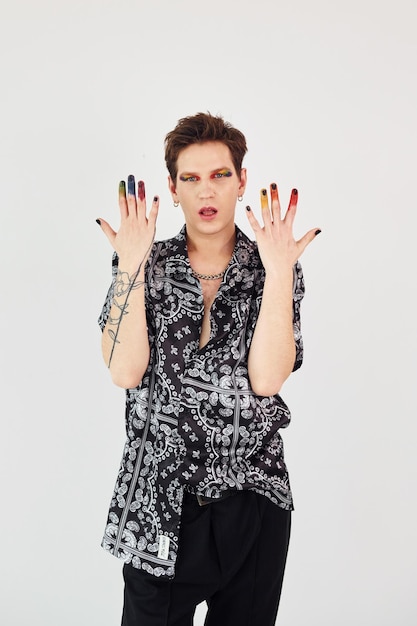 Photo young gay man is standing in the studio and posing for a camera gesturing and doing facial expressions