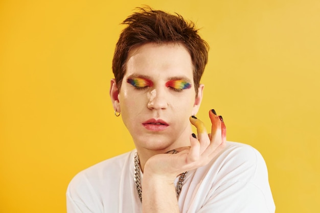 Young gay man is standing in the studio and posing for a camera Rainbow make up