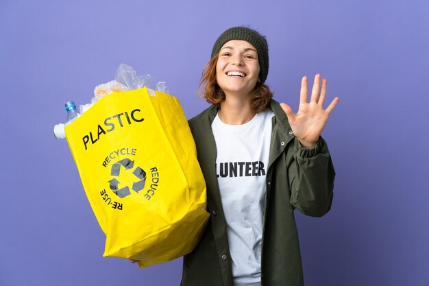 Young Georgian girl holding a bag full of plastic bottles to recycle counting five with fingers