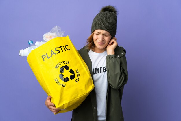 Young Georgian girl holding a bag full of plastic bottles to recycle frustrated and covering ears