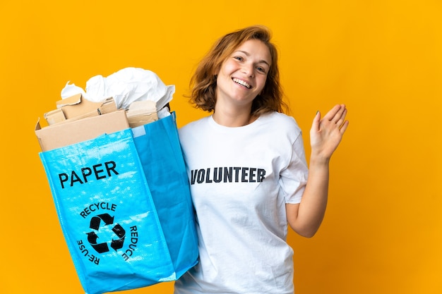 Молодая грузинская девушка держит мешок для переработки, полный бумаги, чтобы перерабатывать, приветствуя рукой с счастливым выражением лица