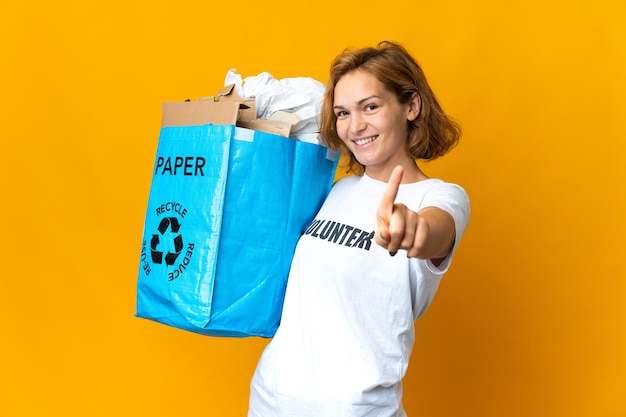 指を見せて持ち上げてリサイクルするために紙でいっぱいのリサイクルバッグを持っている若いグルジアの女の子