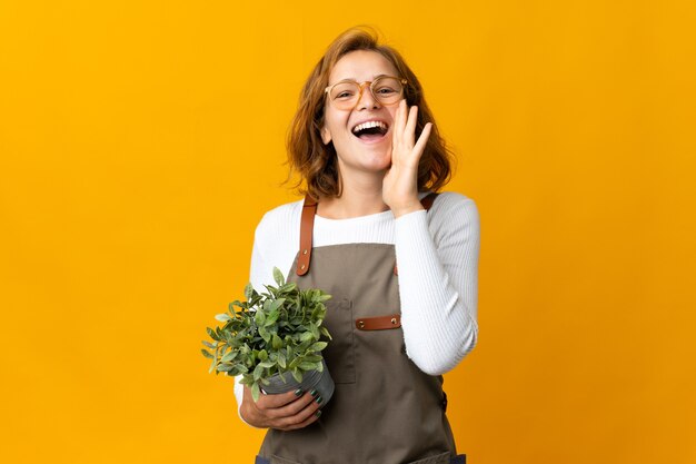 Young Georgian woman holding a plant isolated on yellow background shouting with mouth wide open