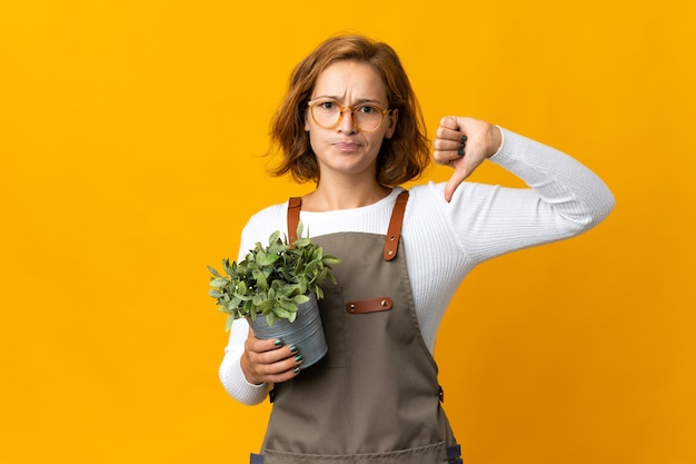 Young Georgian woman holding a plant isolated on yellow wall showing thumb down with negative expression