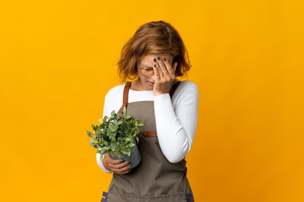 Young Georgian woman holding a plant isolated on yellow wall with tired and sick expression