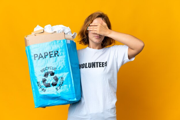 Молодая грузинская женщина держит мешок для переработки, полный бумаги, чтобы утилизировать, прикрывая глаза руками. Не хочу что-то видеть
