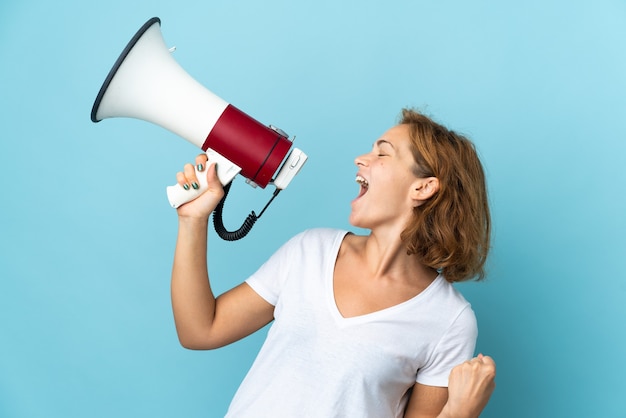 Young Georgian woman isolated on blue background shouting through a megaphone to announce something in lateral position