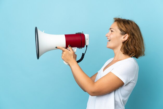 Young Georgian woman isolated on blue wall shouting through a megaphone to announce something