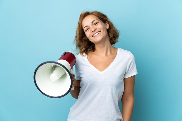 Young Georgian woman isolated holding a megaphone and smiling a lot