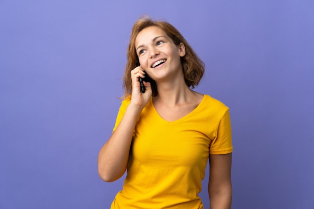 Young Georgian woman isolated on purple background keeping a conversation with the mobile phone with someone