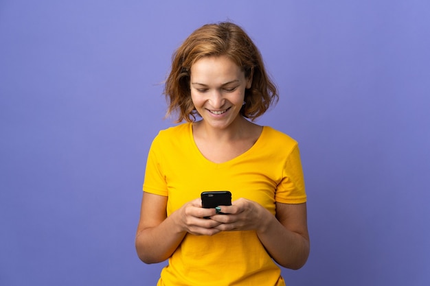 携帯電話でメッセージやメールを送信する紫色の背景に分離された若いジョージ王朝様式の女性