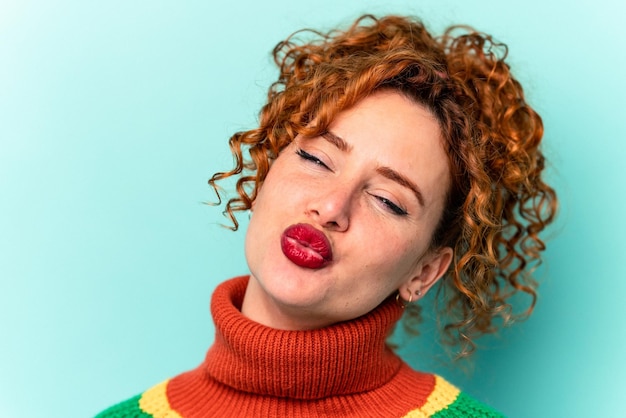 Young ginger caucasian woman isolated on blue background