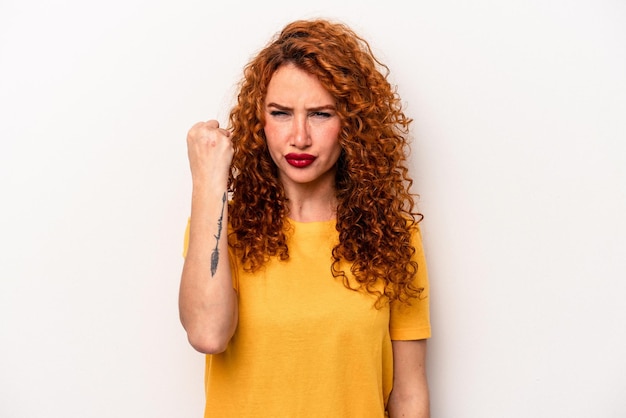 Young ginger caucasian woman isolated on white background showing fist to camera aggressive facial expression