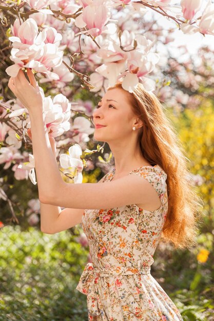 Young ginger hair woman near light pink tender blossoming tree. fairy dreamlike mood of the spring and summer. Beautiful romantic lady smiling bride, wedding. Copy space background.