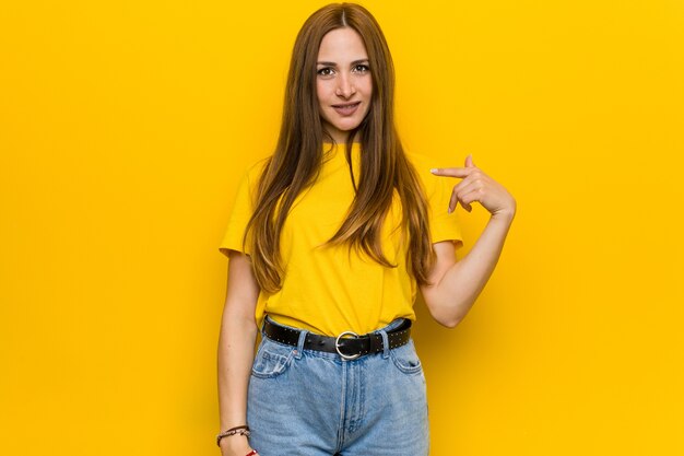 Young ginger redhead woman person pointing by hand to a shirt copy space, proud and confident